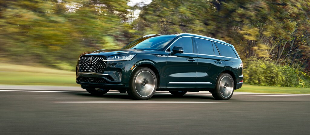 A 2027 Lincoln Aviator® Black Label™ SUV is being driven in a lush countryside