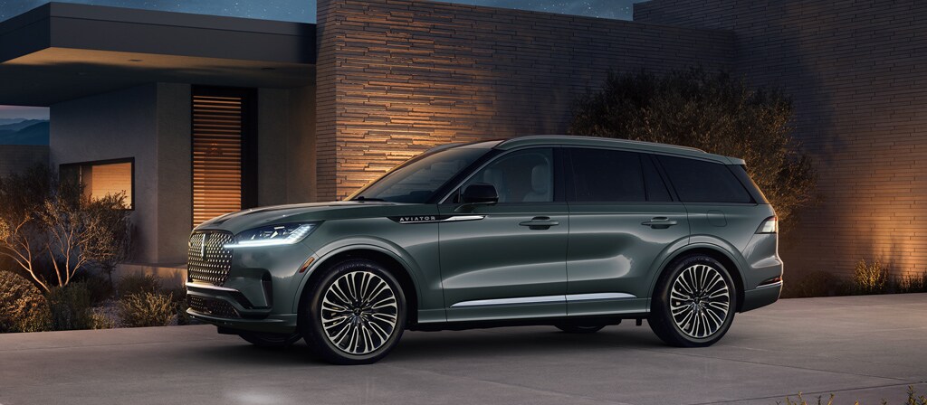 A 2027 Lincoln Aviator® Black Label™ SUV is parked next to a modern home at night