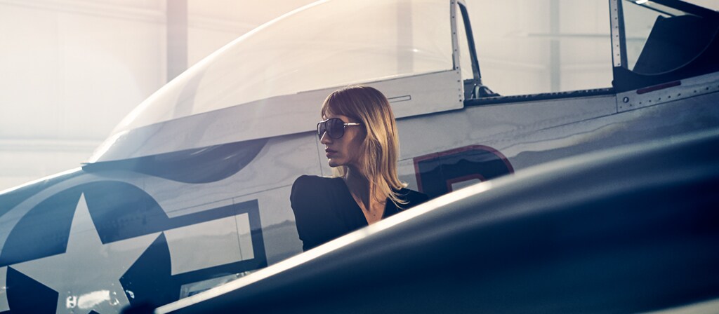A woman walks past a vintage airplane in a private hangar