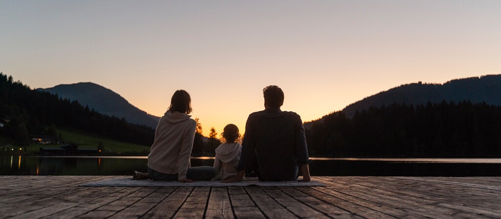 A family sits outdoors at sunset in anticipation of the rising moon
