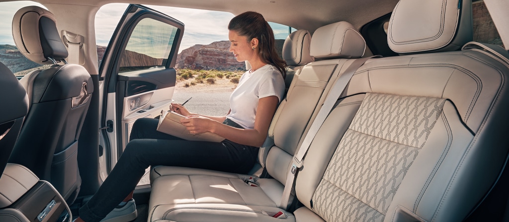 A woman journals in the second row of a Lincoln Black Label™ Nautilus® SUV