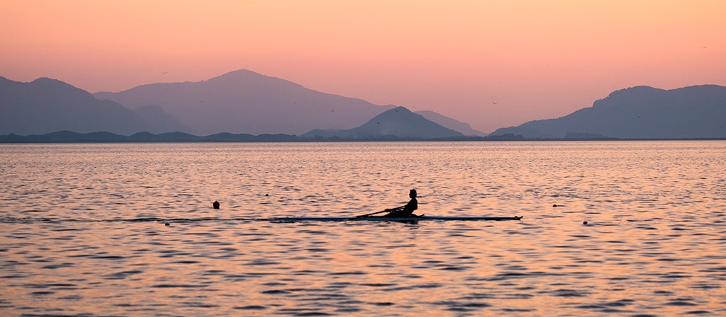 A person rows a scull boat in the ocean in the morning