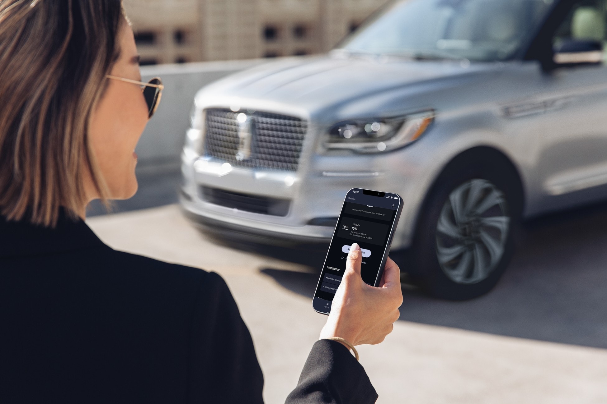 A woman is shown walking to a Lincoln vehicle while holding a mobile device displaying Vehicle Health Alerts.