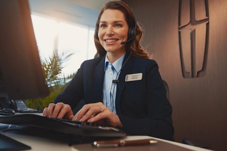 A Lincoln customer service assistant is shown seated at a computer while wearing a headset