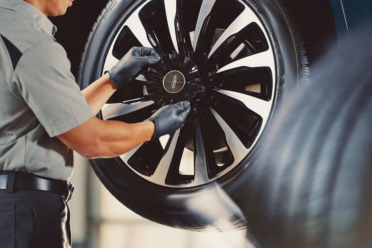 A Lincoln service technician is shown inspecting the tire tread quality of a Lincoln M K Z