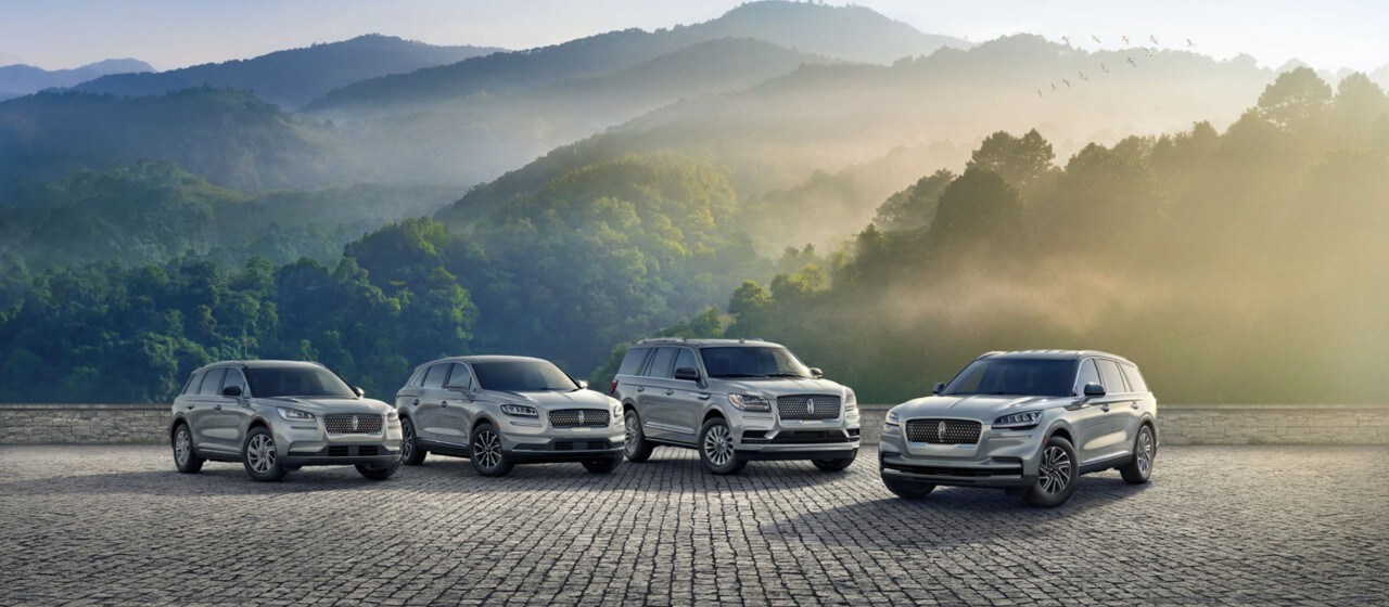 A number of Lincoln vehicles in the Platinum White exterior color are shown parked near a grand staircase