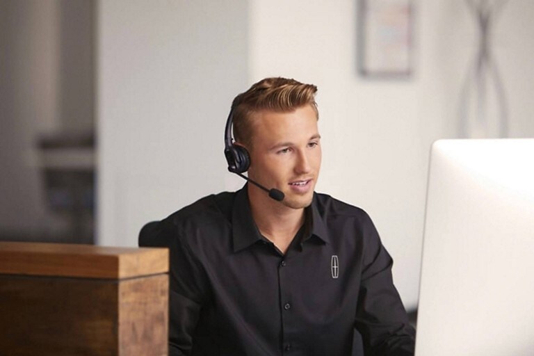 Se muestra un asistente de servicio al cliente de Lincoln en una computadora mientras usa un audífono