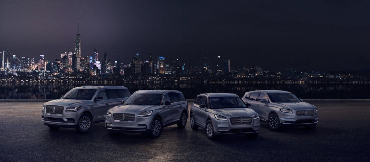 A group of Lincoln vehicles are parked together against the city landscape