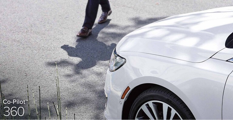 Un vehículo Lincoln blanco se detiene delante de un peatón para demostrar el funcionamiento de la característica de asistencia antes de una colisión con frenado automático, la cual forma parte de Co-Pilot360