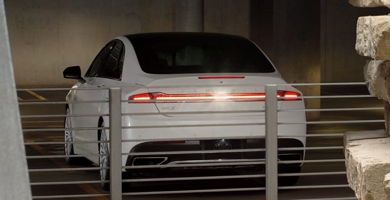 Un Lincoln MKZ blanco retrocede en un estacionamiento para demostrar la característica de los sistemas de detección de marcha atrás/adelante
