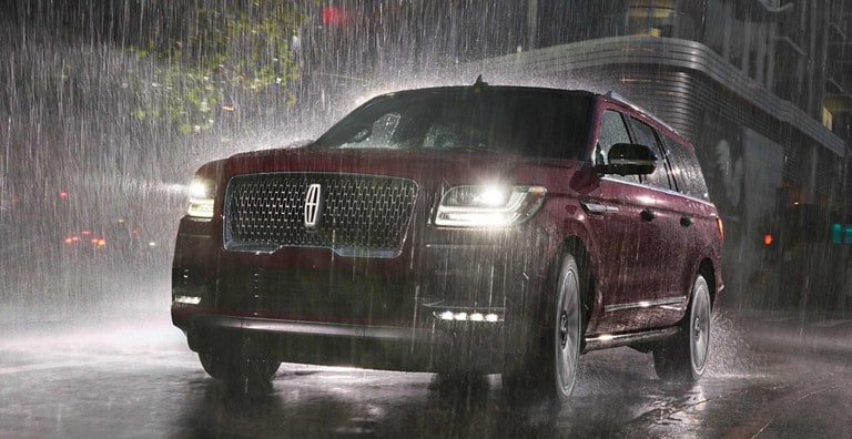 Una Lincoln Navigator en rojo durante la noche y bajo la lluvia usando los limpiaparabrisas con sensor de lluvia