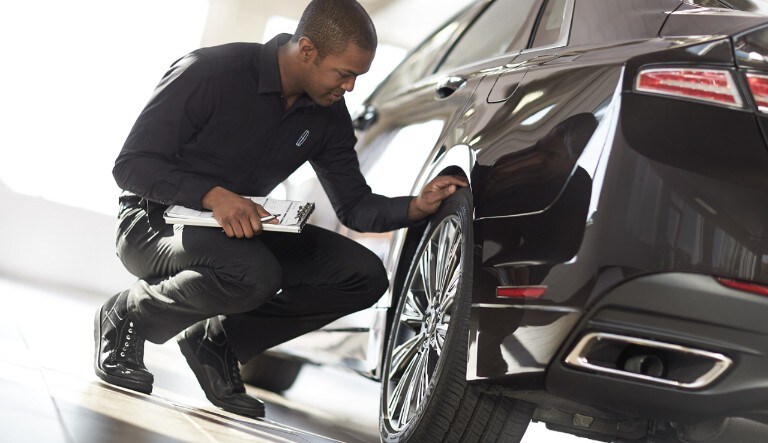 Man inspecting rear tire on a black Lincoln MKZ