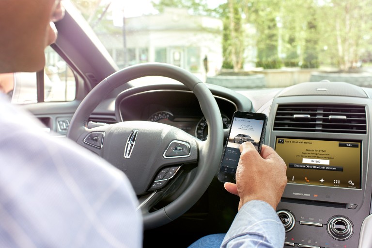 The driver holds his mobile device, connecting to the Lincoln Connect hotspot.