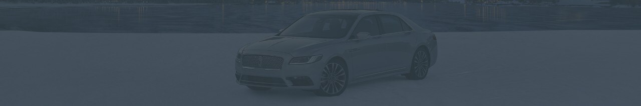 A Lincoln Continental is parked in front of a calming body of water