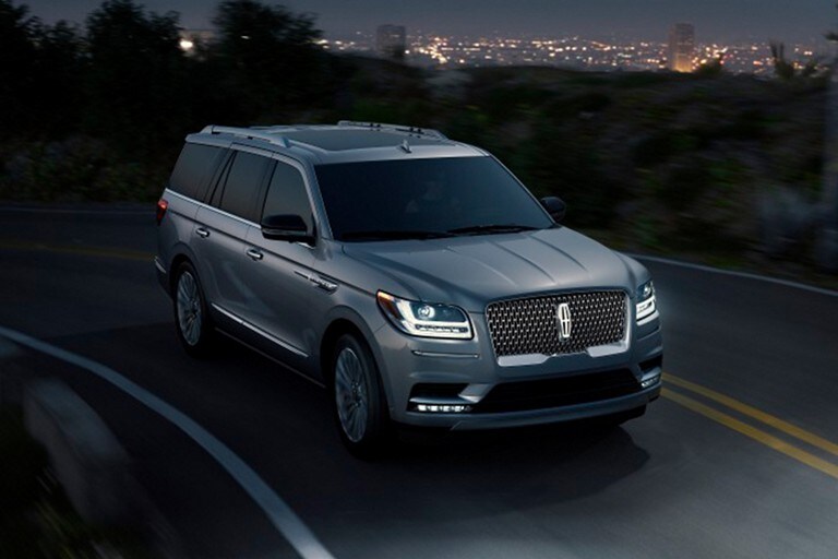 Bright L E D adaptive headlamps light the road ahead in dramatic contrast to the dark night and twinkle of city lights within the backdrop