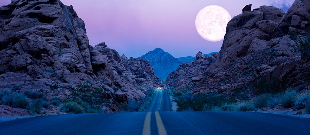 The moon rises above a desert southwest highway at night