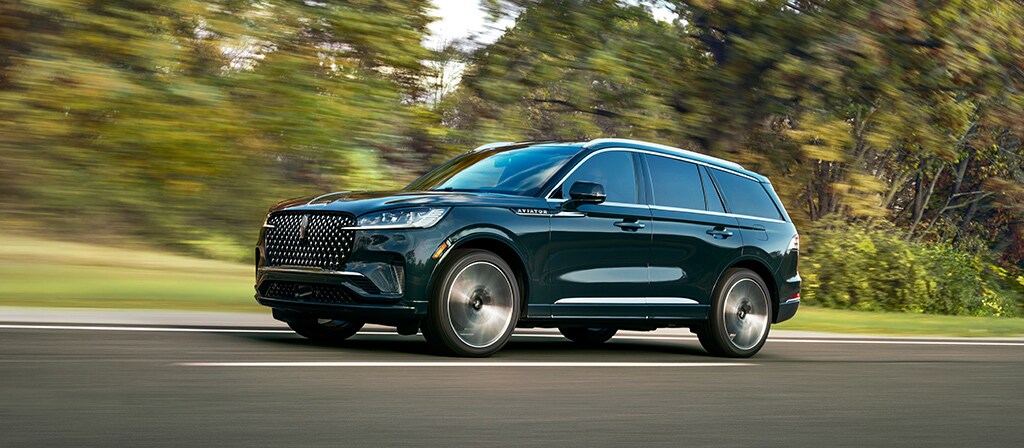 A 2026 Lincoln Aviator® SUV is shown driving on a forested road
