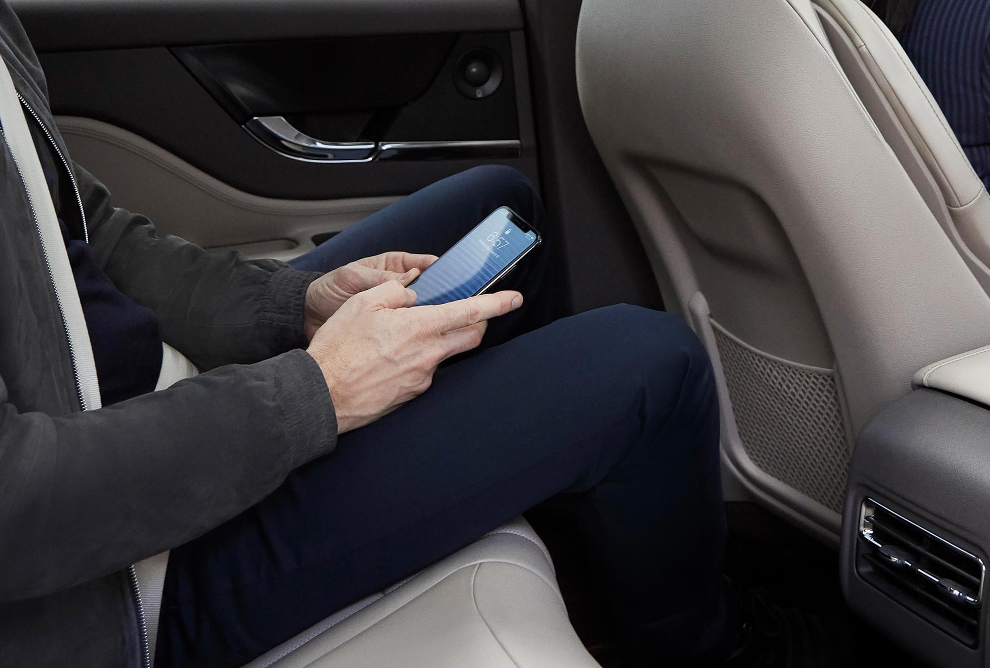 A man holding a smart phone in the backseat of a Lincoln Corsair.
