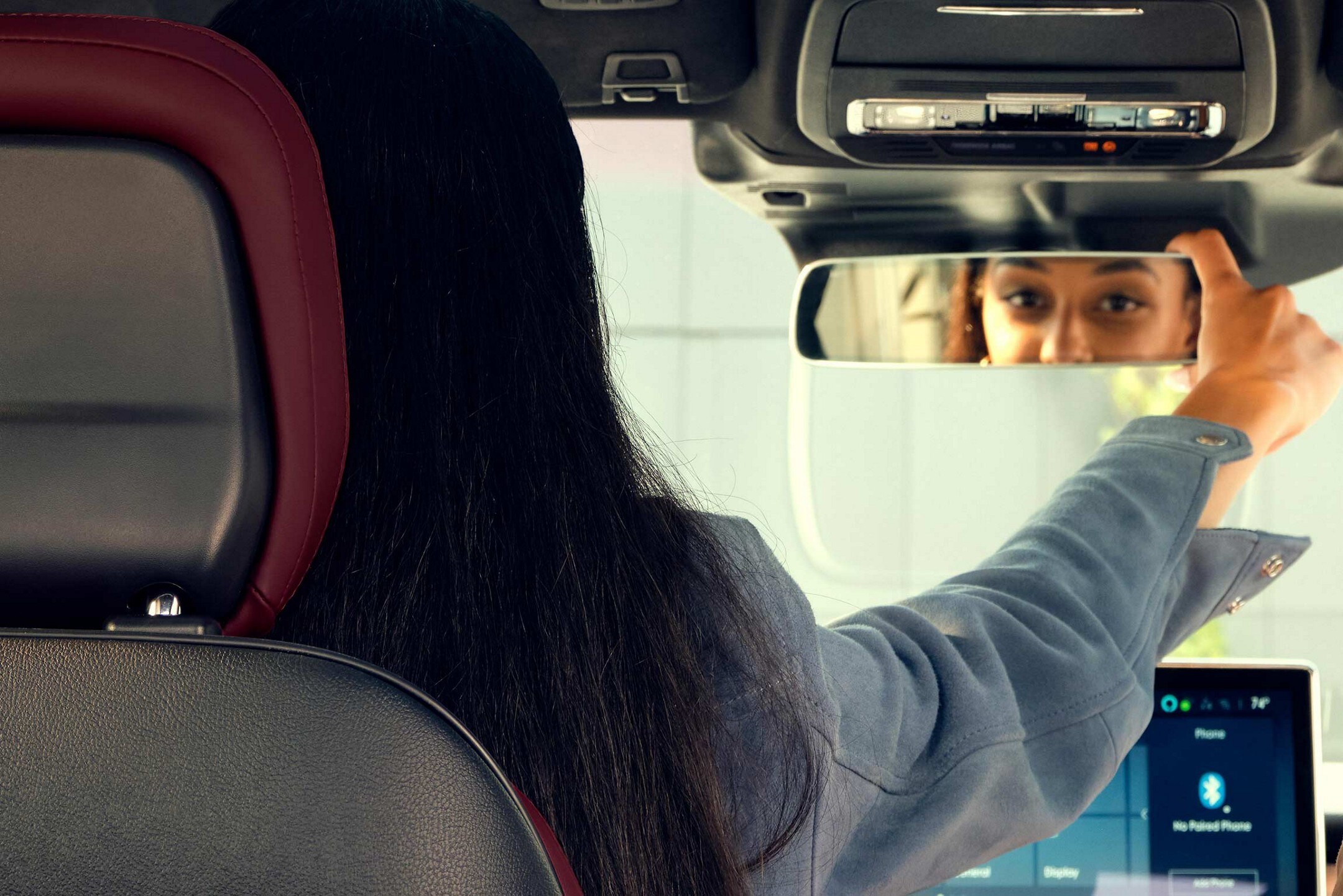 A woman adjusting the rear-view mirror.