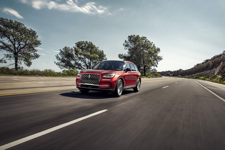A 2024 Lincoln Corsair® SUV in Crystal Red drives on a tree-lined road