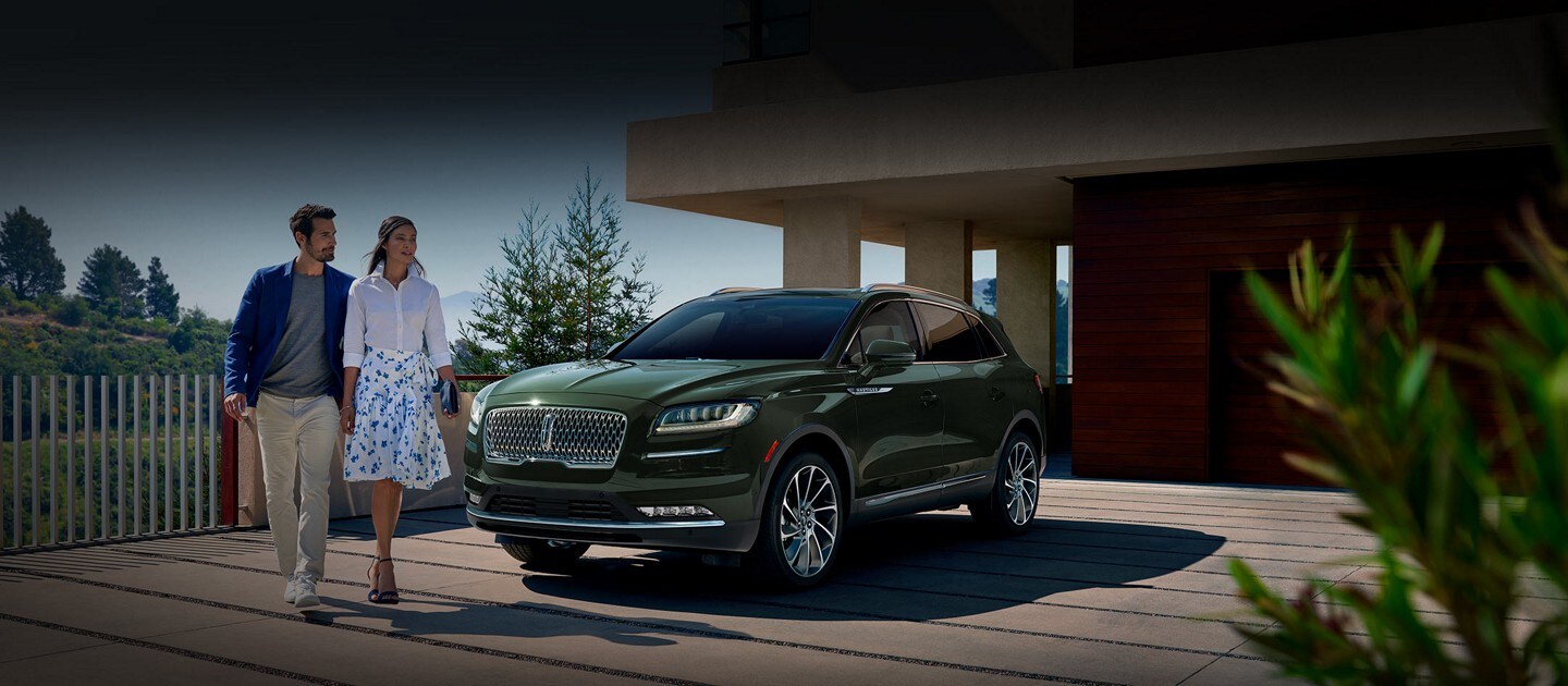 A 2023 Lincoln Nautilus® SUV shown in the Gilded Green exterior color is parked in the driveway of a modern hillside home