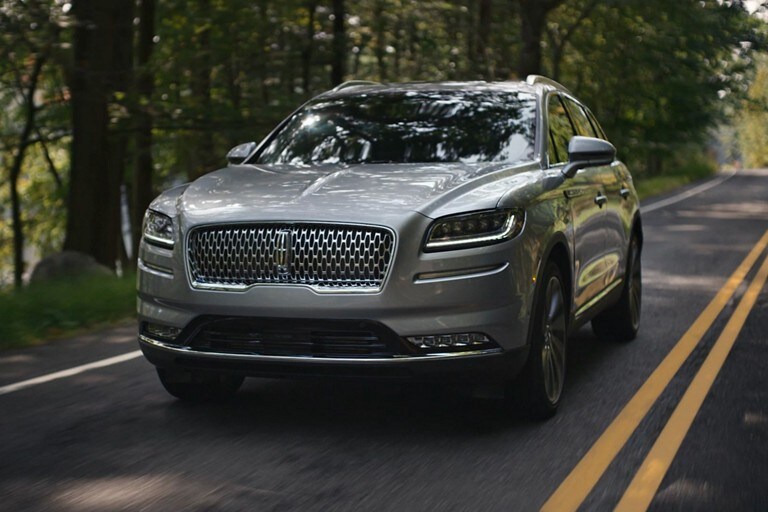 Se muestra una pareja acercándose a una SUV Lincoln Nautilus® en un pintoresco entorno de montaña