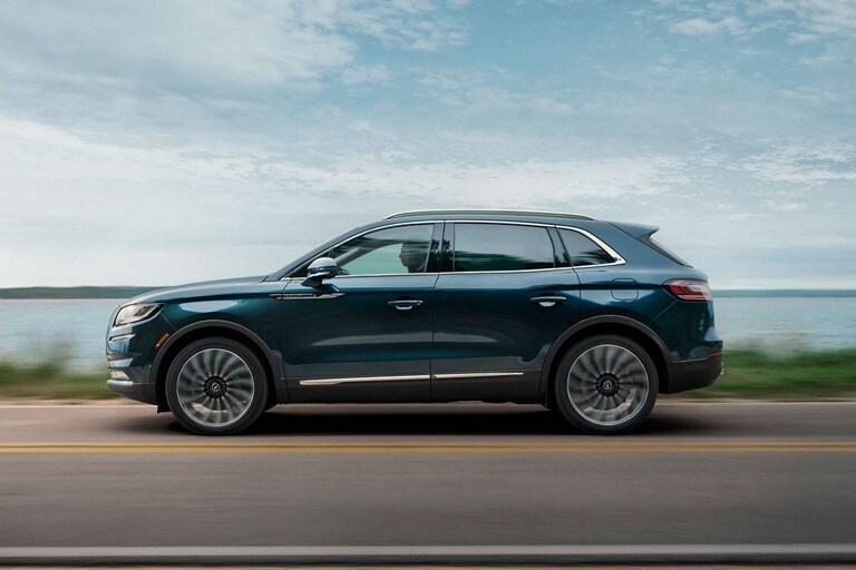 Una SUV Lincoln Black Label Nautilus® 2023​​​​​​​ andando por un camino junto a un lago