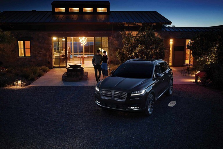 El tapete de bienvenida con logo Lincoln se proyecta en el suelo al lado de la puerta del conductor de una SUV Lincoln Nautilus® 2023