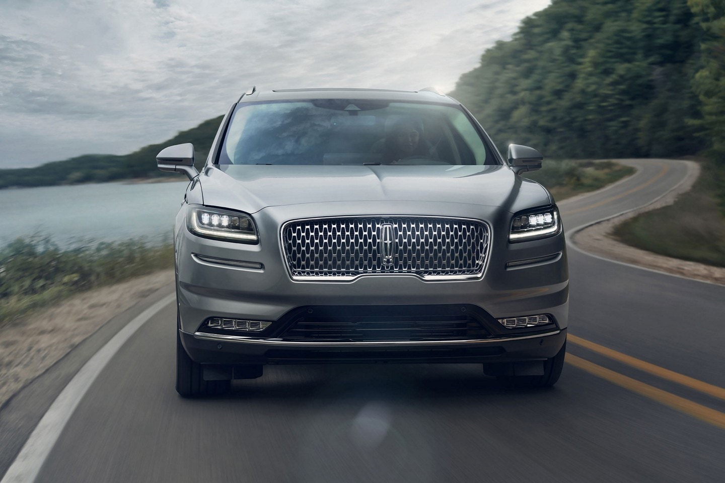 La SUV Lincoln Nautilus® 2023 circulando por una curva en una carretera junto a un lago