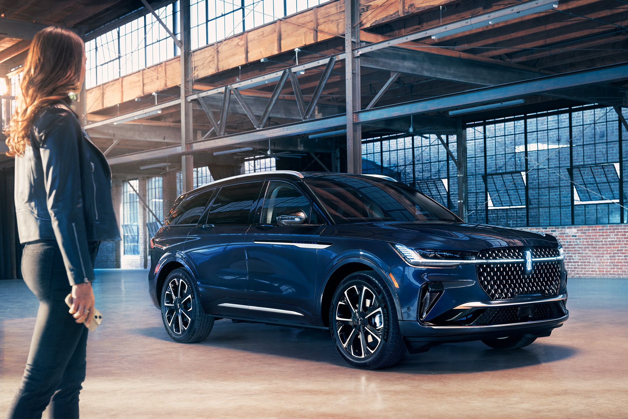 A smartphone is being held in a woman’s hand as she walks toward a 2024 Lincoln Premiere Nautilus® SUV.