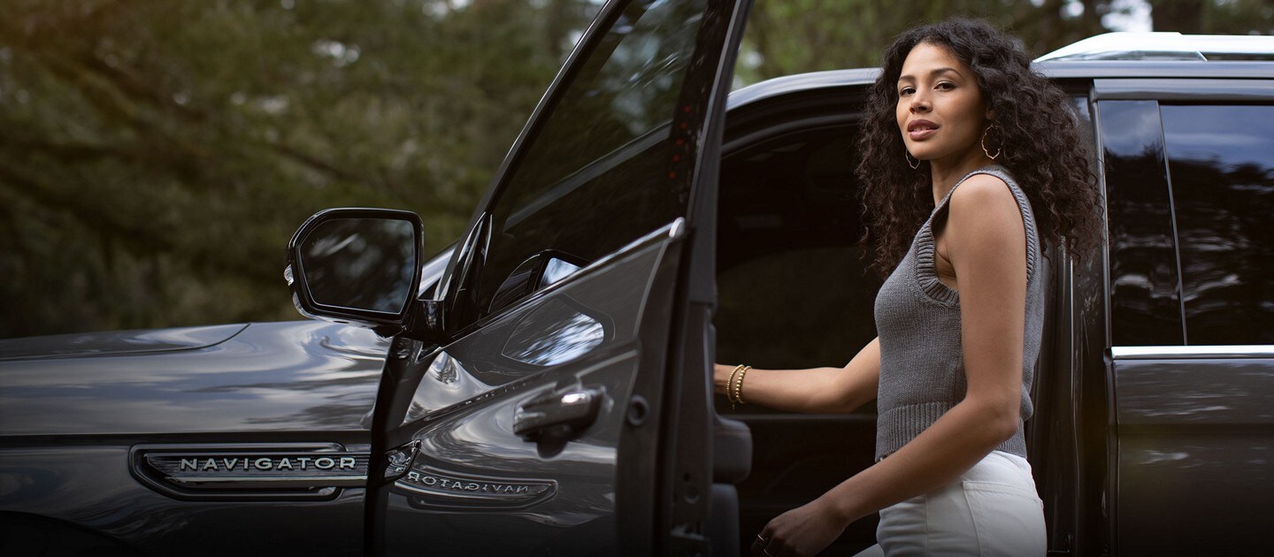 A beautiful woman is getting into the driver’s seat of a 2024 Lincoln Black Label Navigator® SUV in Chroma Caviar Dark Gray.