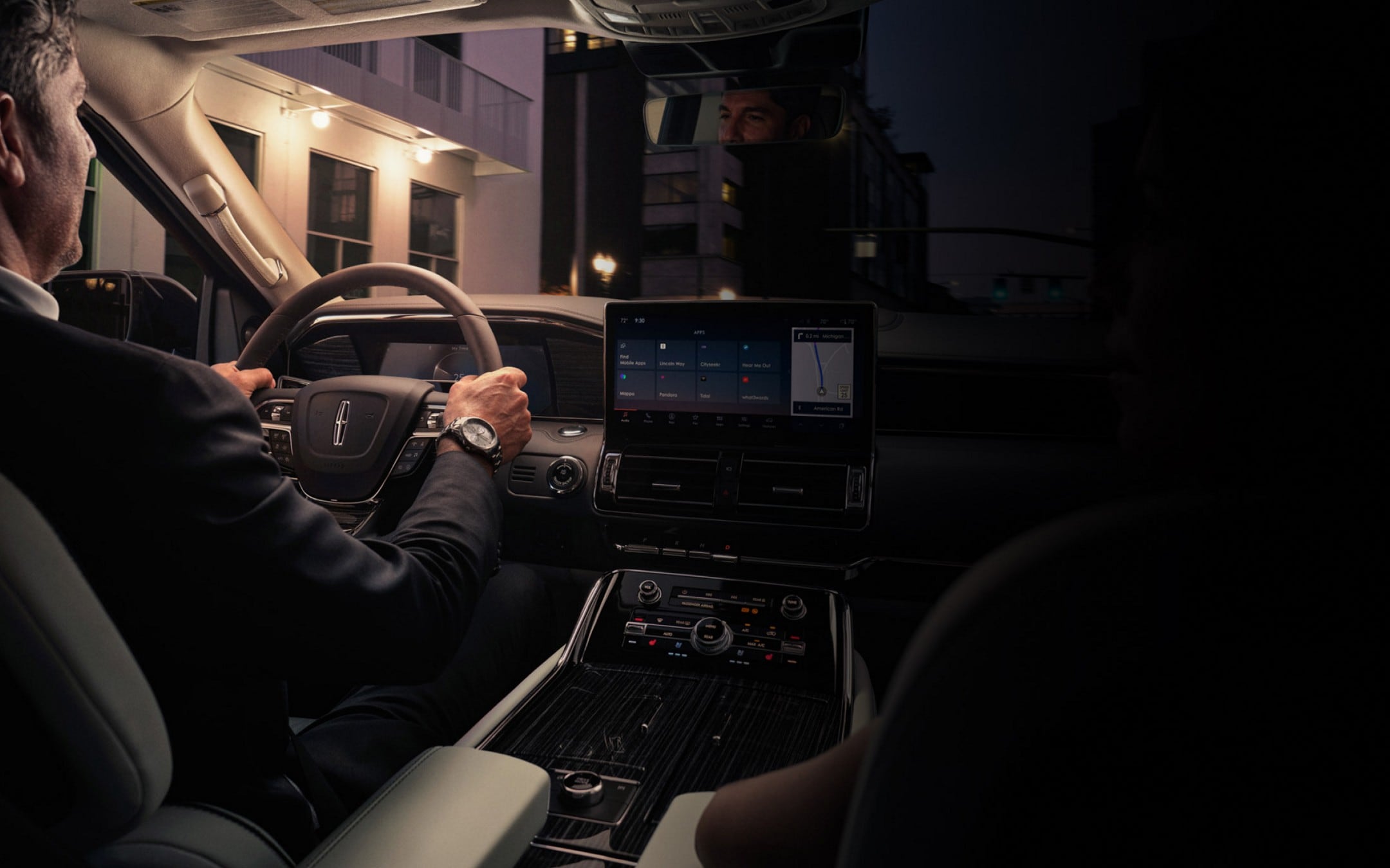 Un hombre se relaja en el interior de una SUV Lincoln Navigator® 2024 mientras conduce por una calle céntrica de una ciudad por la noche
