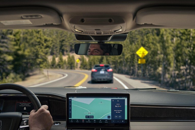 Through the windshield we see a vehicle braking ahead as it is driven around a sharp turn on a mountain pass.