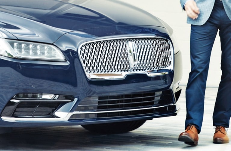 Man with blue pants and brown shoes walking in front of a blue Lincoln Continental