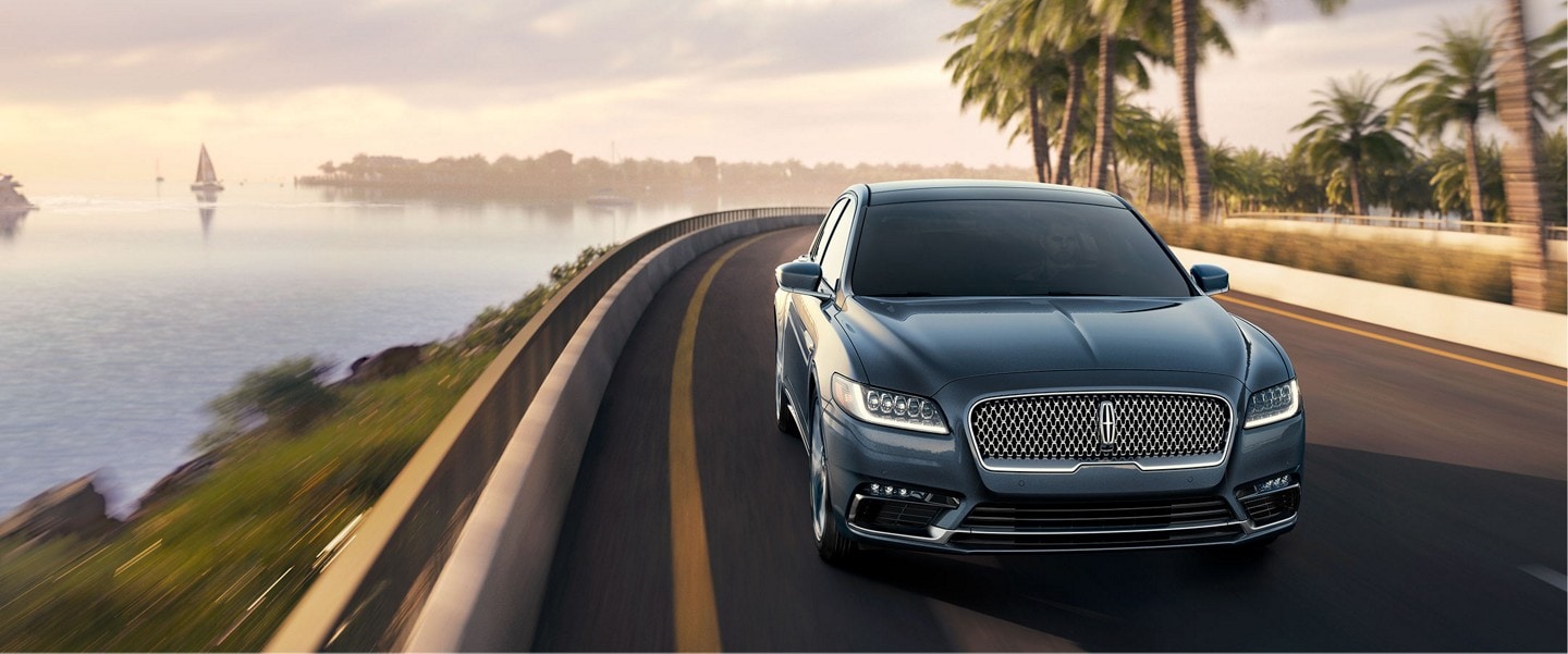 Luxurious black Lincoln Continental driving on the open road next to the water on one side and palm trees on the other