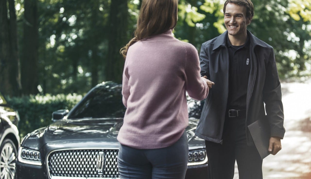 Woman greeting a man in front of a grey Lincoln Continental