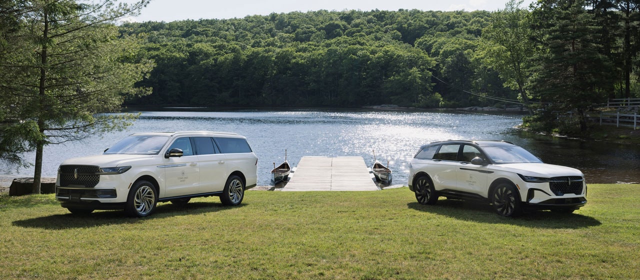 Two Lincoln vehicles parked on a lawn infront of a lake.