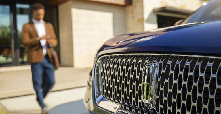 A man is shown approaching a Lincoln vehicle as he uses his smartphone