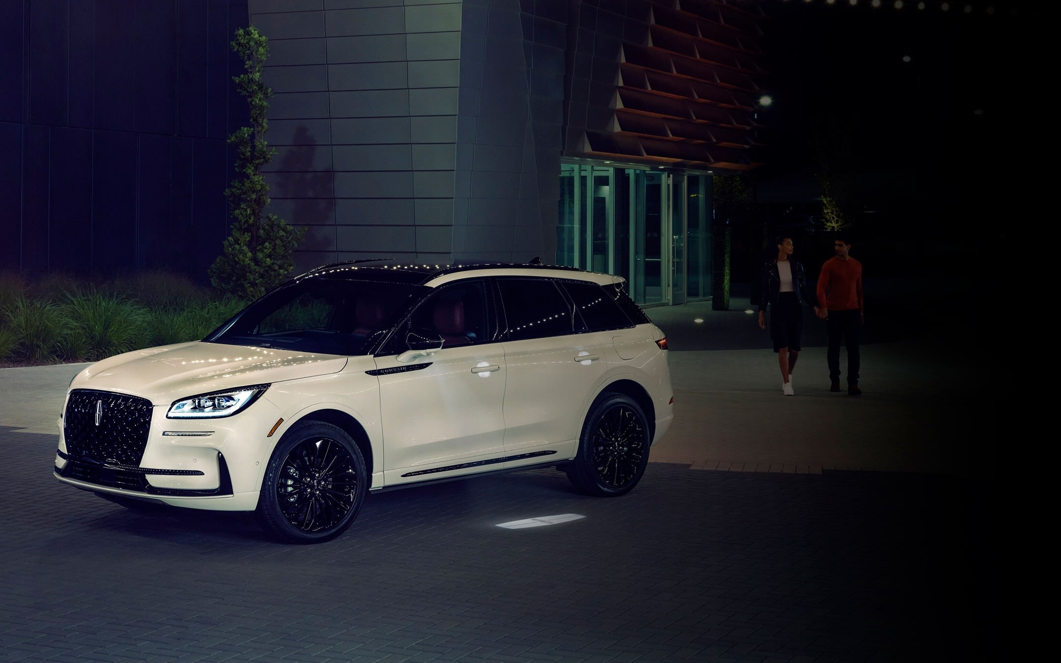 A couple approaches a 2025 Lincoln Corsair® Reserve model as the Lincoln Embrace illumination guides the way