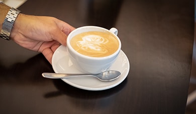 A host serves a complimentary cappuccino to a guest.
