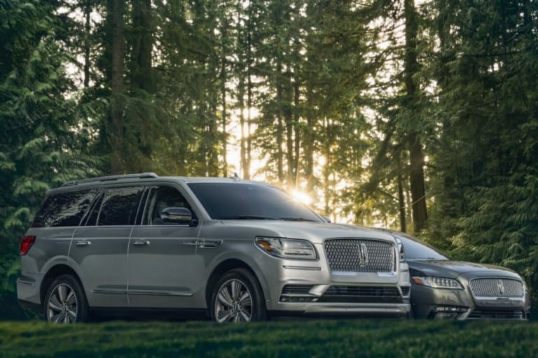 Lincoln Navigator y Continental 2018 en plateado lingote estacionados sobre césped cerca de árboles altos