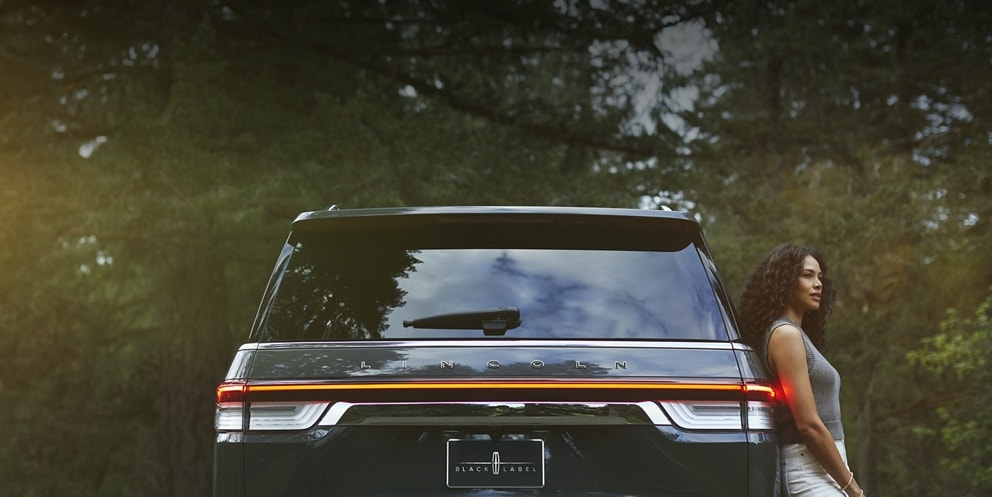 a woman leaning against a Lincoln vehicle is shown here