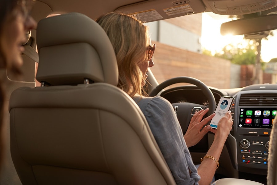 A woman is shown sitting in the drivers seat of a Lincoln M K C as she downloads an app on her mobile phone.