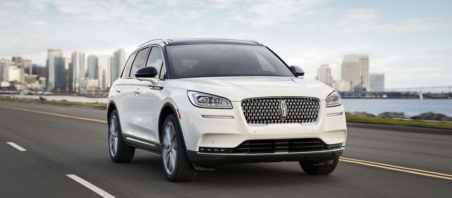 A Lincoln Corsair in pristine white is effortlessly driving along a coast using Lincoln Drive modes.