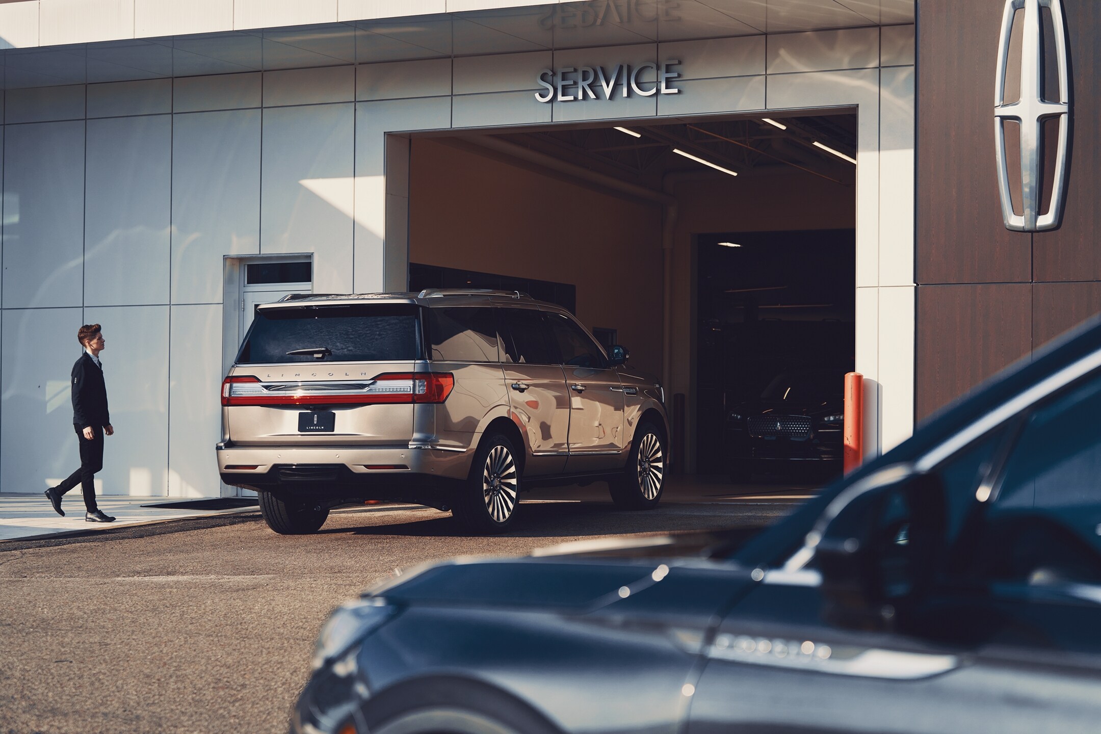 A Lincoln vehicle driving into the service center at a Lincoln retailer.