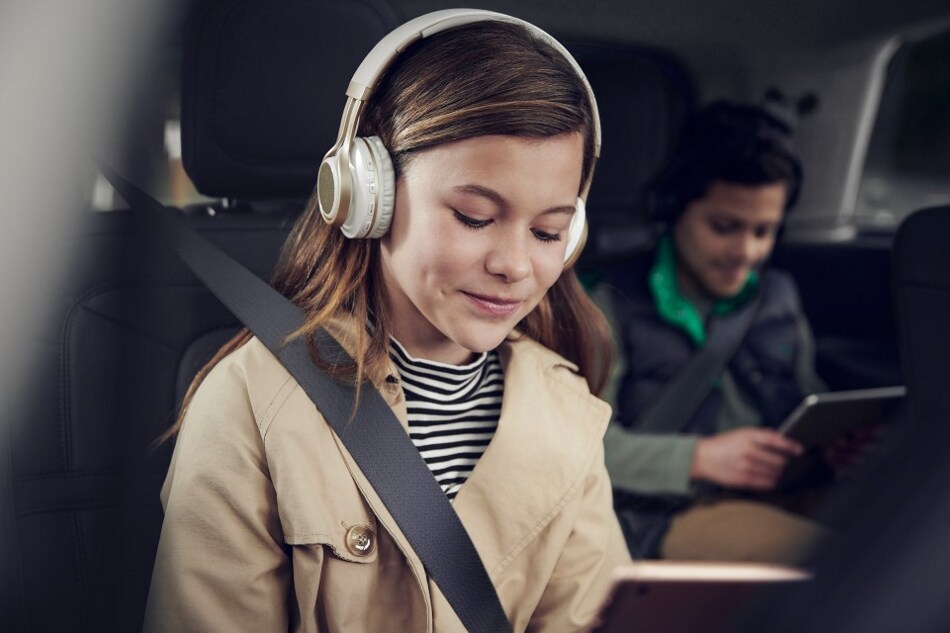 Two children are shown in the front and second-row seats of a Lincoln vehicle while looking at tablet devices and wearing headphones.