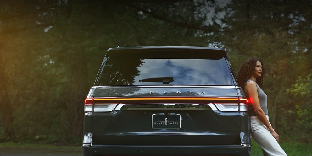 Una mujer se relaja contra el costado de una SUV Lincoln Black Label Navigator® 2023.