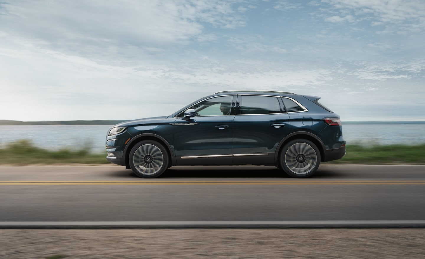     A 2023 Lincoln Nautilus® SUV is being driven on a road near a lake