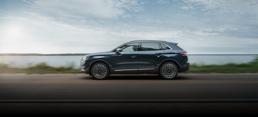 Una SUV Lincoln Nautilus® 2023 que se desplaza por una carretera cerca de un lago