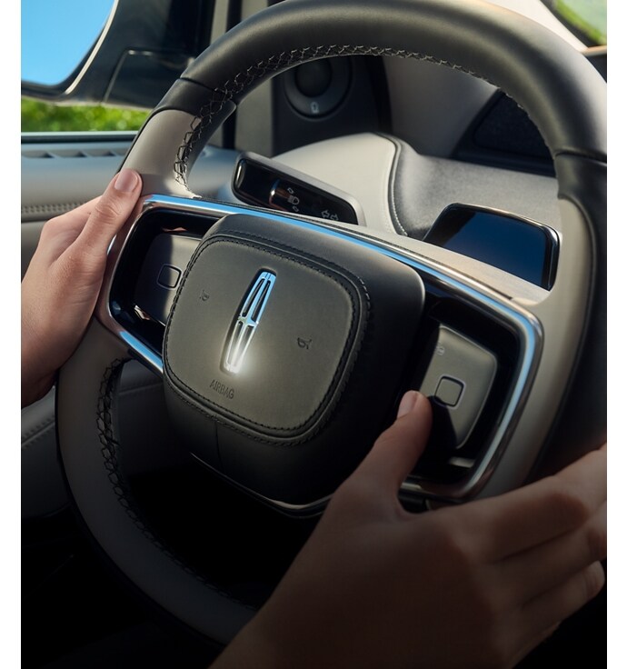 A man holding the steering wheel inside a Lincoln vehicle.